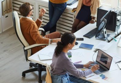 Coworkers collaborating in a bright open-plan office with white desks and large windows.