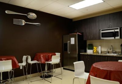 Modern breakroom with dark cabinetry, red tablecloths, and large decorative wall utensils.