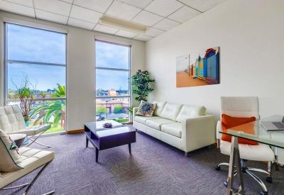 Bright office lounge area with white leather sofa and colorful wall art.