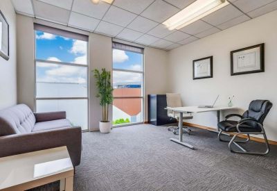 Bright private office featuring a grey sofa, desk, and large windows.