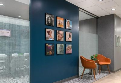 Reception seating area with orange armchairs and a gallery wall of framed portraits.