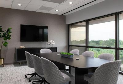 Conference room featuring a dark oval table, grey quilted chairs, and large windows.