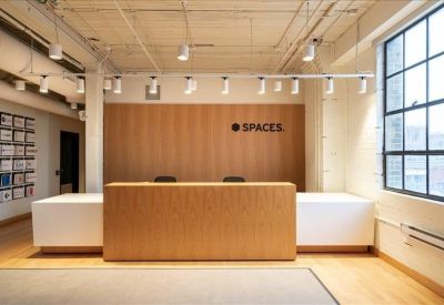 Minimalist wood-fronted reception desk with overhead track lighting and 'SPACES' logo.