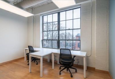Bright corner workstation with two white L-shaped desks and black mesh office chairs.