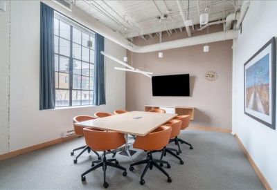 Meeting room with industrial windows, large white table, and orange swivel chairs.