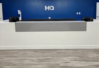 Modern white reception desk with gray accents in front of a blue wall featuring a company logo.