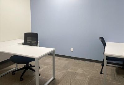 Private office featuring white L-shaped desks, black mesh chairs, and a blue feature wall.