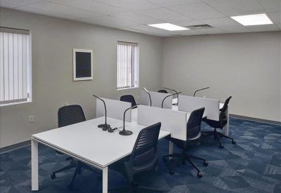 Spacious coworking area with multiple white desks, black chairs, and desk lamps on a blue patterned carpet.