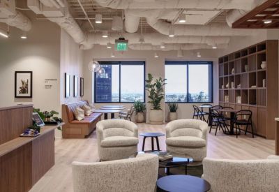 Spacious coworking lounge with mid-century modern armchairs and city views through large windows.