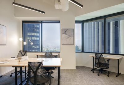 Bright shared office space with ergonomic chairs and wooden desks near floor-to-ceiling windows.