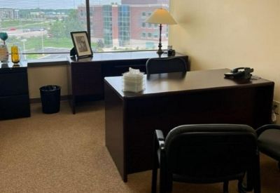 Private office suite with a dark wood desk, guest seating, and large windows with a city view.
