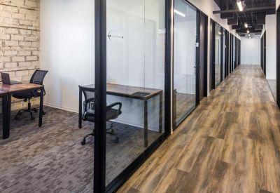 Hallway view featuring private glass-enclosed offices with wood-style flooring and exposed brick.