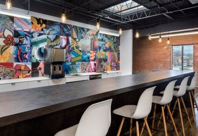 Long communal bar table with white stools set against a vibrant multi-colored wall mural.