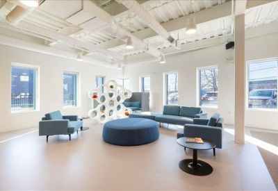 Spacious communal lounge with blue sofas, a round ottoman, and large windows.