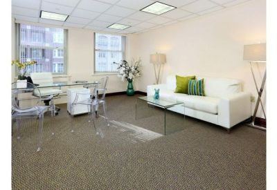 Bright breakout lounge with a white sofa, green accent pillows, and transparent chairs.