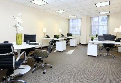 Open-plan workspace with multiple white desks, black task chairs, and large windows.