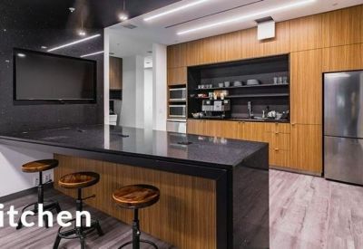 Modern office kitchen featuring a large black island, wooden cabinetry, and stainless steel appliances.