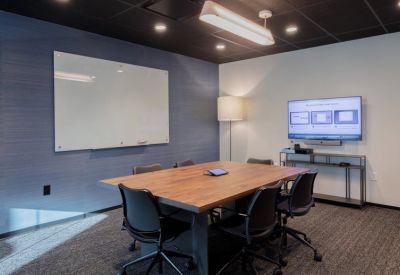 Meeting room with a large wood table, black ergonomic chairs, and a digital presentation screen.