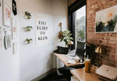 Workstation nook with a wooden desk, potted plants, and an exposed red brick wall.