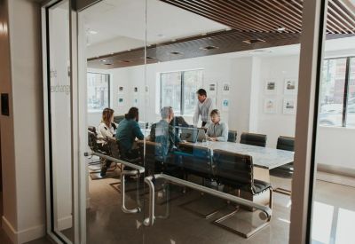 Bright conference room with a long glass table and black chairs viewed through glass doors.