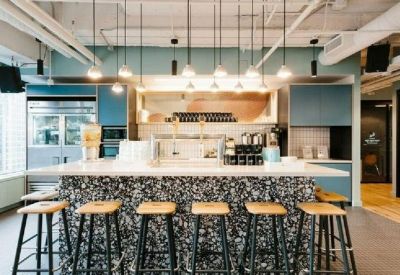 Modern office kitchen area with a stone-textured island, blue cabinetry, and hanging pendant lights.