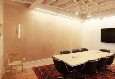 Modern conference room with a large table, black chairs, and light wood wall panels.