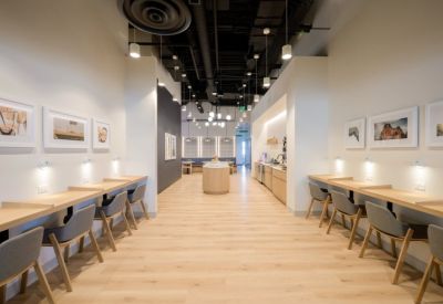 Long coworking hall with wooden desks, grey chairs, and a central kitchen island.