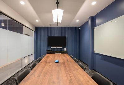 Professional boardroom featuring a long wood table, blue accent wall, and large screen.