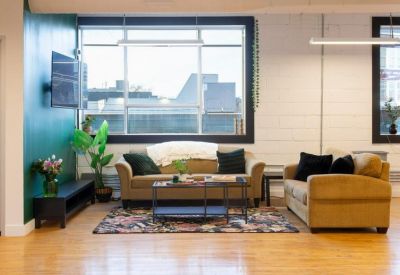Bright communal lounge with tan sofas, a patterned rug, and a large window.