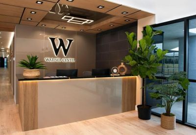 Modern reception area with a branded desk, wood accents, and large fiddle leaf figs.