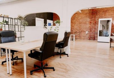 Open-plan office with multiple workstations, black chairs, and large brick archways.