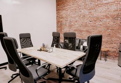 Professional meeting room with a light wood table, black mesh chairs, and a brick feature wall.