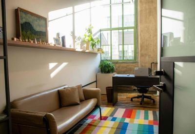 Cozy lounge area with a leather sofa and colorful geometric rug near a private desk.