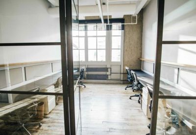 Bright glass-partitioned private office with wooden flooring and natural light.