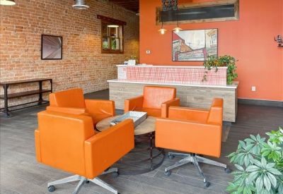 Reception area with a light wood front desk and orange lounge chairs.