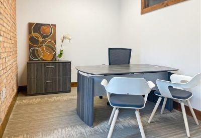 Private office featuring a grey desk, black chair, and brick accent wall.