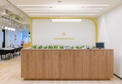 Bright reception area with a wooden front desk and Industrious branding set against a white wall.