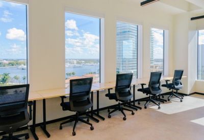 Long wooden hot desk area with black mesh chairs facing large windows with water views.