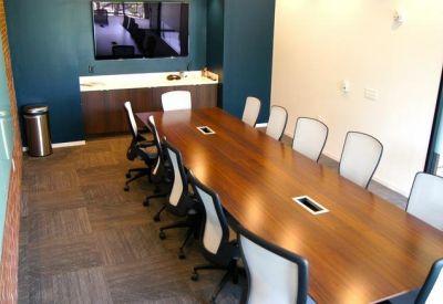 Long wooden boardroom table with mesh chairs and a wall-mounted TV.