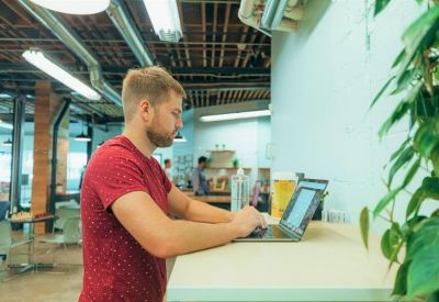 Professional working at a standing desk near a white brick wall with greenery.