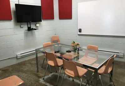 Meeting room with a glass-top table, orange chairs, and a wall-mounted TV screen.
