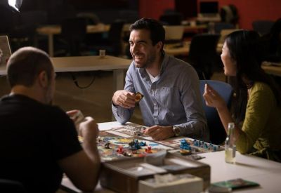 Casual coworking space with people sitting around a table playing a board game.