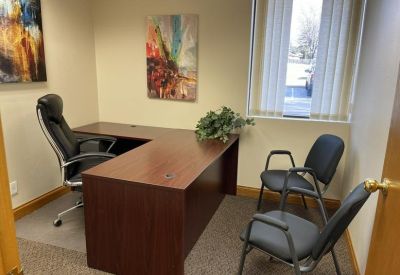 Private office featuring a dark wood L-shaped desk and guest chairs near a window.