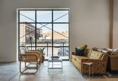 Modern lounge area with a patterned sofa and wicker chairs in front of a large industrial window.