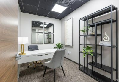 Bright private office suite with a white desk, grey armchair, and a tall black shelving unit.