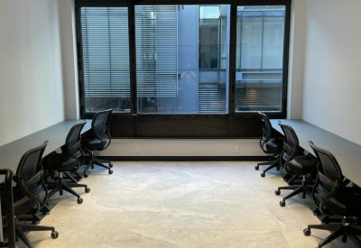Modern office suite with two rows of desks and black ergonomic chairs facing large windows.