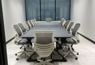 Spacious boardroom with a long black table and white mesh chairs under a slatted ceiling.
