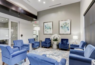 Spacious communal lounge area with plush blue armchairs and floral wall art.