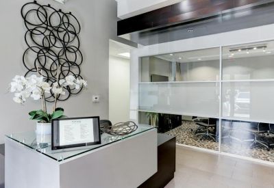 Modern reception area with a white front desk, glass partitions, and decorative wall art.