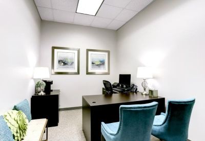 Private office featuring a dark wood desk, framed artwork, and blue velvet armchairs.
